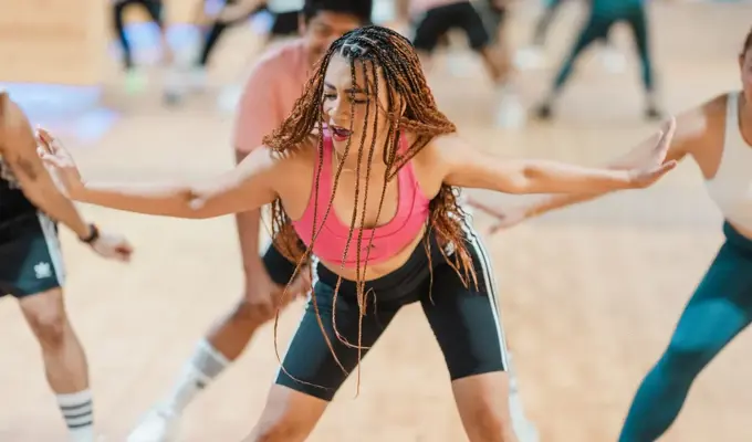 GN-Women leading a high-energy Zumba class at GymNation, dancing in a colorful studio with other participants in the background